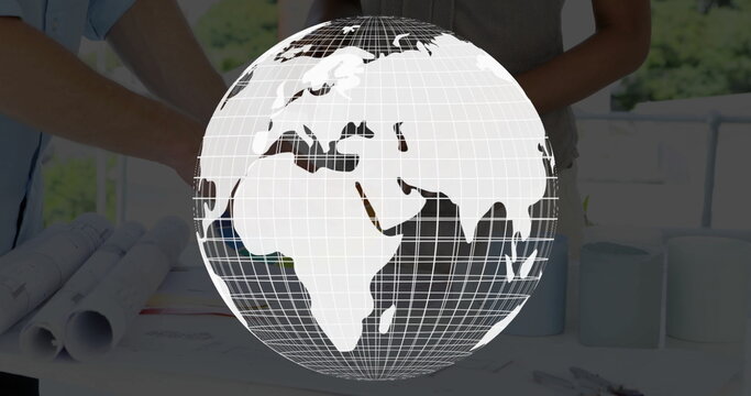 Displaying wireframe globe over studio desk, with colleagues reviewing architectural blueprints - Powered by Adobe