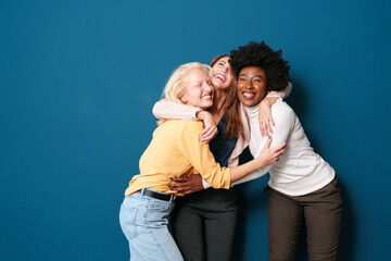 Multicultural Female Friends Sharing Genuine Laughter Moment in Casual Attire Against Turquoise Wall