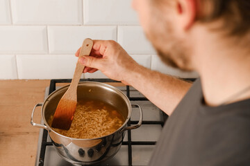 Man cooking ramen noodles. Male making noodle soup broth in the home kitchen stove. Traditional Asian food. Close Up Photo Of Mans Hands Serving Pasta With Fresh Vegetables. Preparing Homemade Dish.