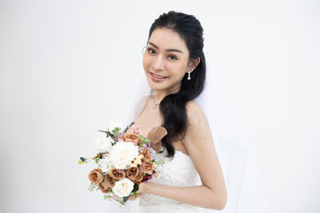 Asian beautiful bride smiling happily holding bouquet of flowers in white wedding dress against...