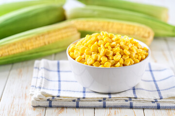 White ceramic bowl with canned food maize on a light kitchen table, selective focus.