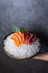 Raw salmon and tuna sashimi served in a bowl with ice on a dark background