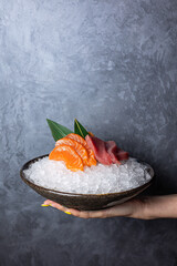 Raw salmon and tuna sashimi served in a bowl with ice on a dark background
