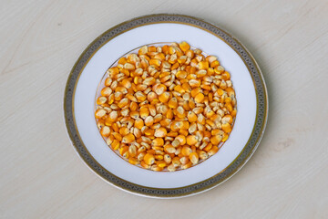Raw corn seeds, Zea mays, in white ceramic plate on wooden background. Fresh sweetcorn kernels, also known as maize.