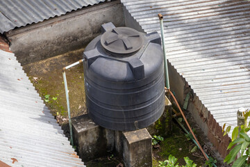 Black plastic water tank on a village house rooftop in Bangladesh. Water storage with connected pipeline, mossy surface, concrete roof from above.