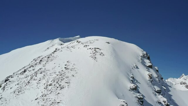 Aerial drone footage of snow-covered Mount Cheget and Mount Elbrus under a clear blue sky, showcasing pristine slopes, rugged peaks, and serene winter majesty
