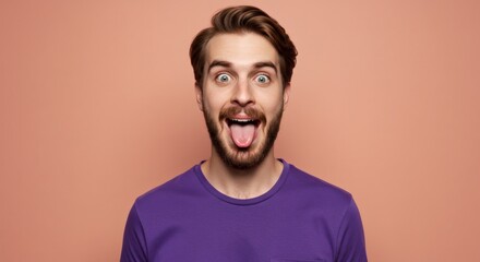 Obraz premium Playful man with beard sticks out tongue playfully against peach background expressing fun and joy in a casual portrait