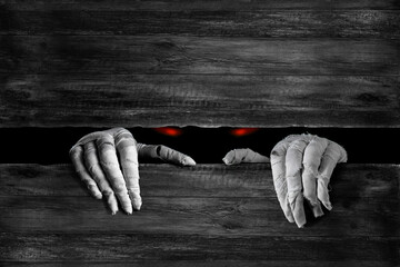 Mummy's hands wrapped in bandage rises through wooden boards. Background with copy space. Horrible glowing eyes stare out of the darkness of the risen dead mummy monster for Halloween horror concept .