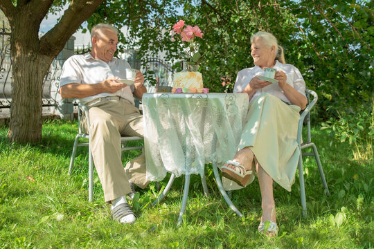 Elderly woman and retired man having breakfast together outdoors in summer. Happy active senior couple having fun in their garden on a picnic