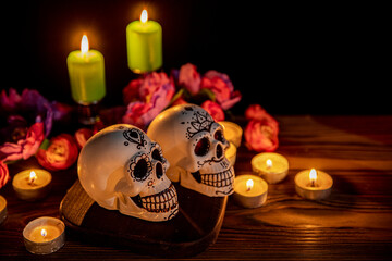 Skulls with decor for the holiday Day of the Dead. Dia de los Muertos altar surrounded by ornamented calavera, candles, flowers in the darkness. All Saints' Day evening