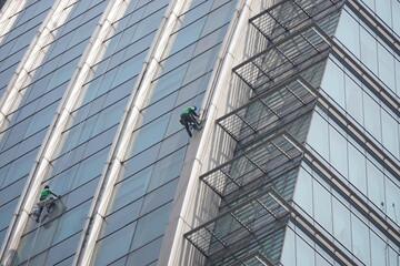 Obraz premium Window cleaners working on the facade of a modern high-rise building. Industrial abseilers wearing safety harnesses while cleaning the glass exterior of a skyscraper in the city.
