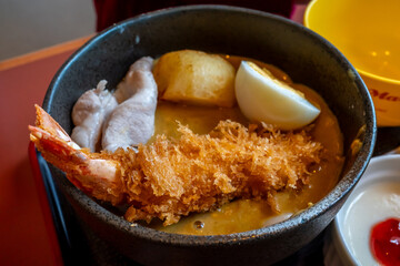 Deep fried shrimp in Japanese style, ebi katsu, in curry soup with boiled egg and pork, in black bowl in local Japanese restaurant