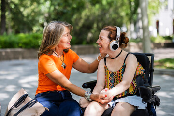 Happy senior woman supporting her disabled daughter in a wheelchair in a park