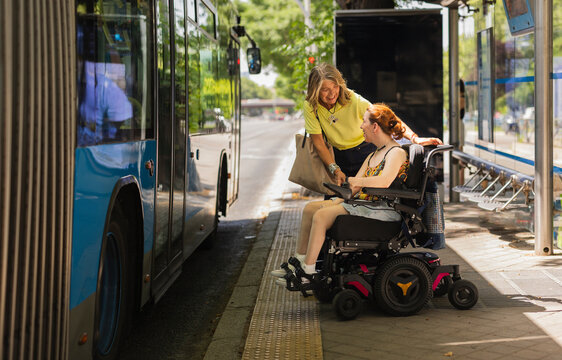 Woman helping disabled girl on wheelchair to board bus at bus stop - Powered by Adobe