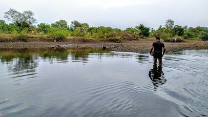 A person standing in a shallow body of water, likely a river or a stream, with lush green...