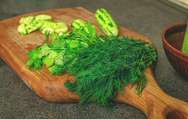 Freshly chopped cucumbers and a bunch of green herbs rest on a rustic cherry wood cutting board....
