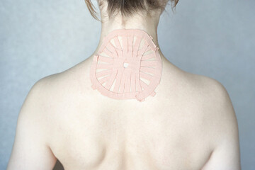 Female adult caucasian back with therapeutic tape applied for pain relief and muscle support.