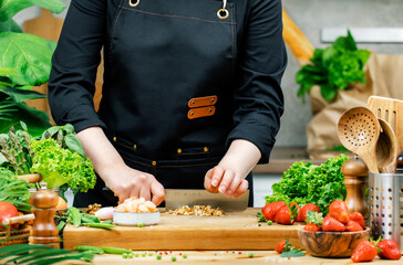 female chef blogger chops walnuts and fresh vegetables on wooden cutting board in kitchen with...