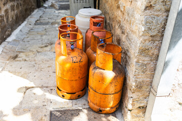 Old gas cylinders stand in a narrow stone alley under the summer sun. Urban infrastructure, fuel storage, and rustic street atmosphere