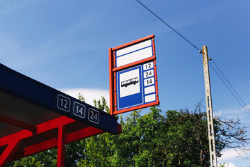 Bus stop sign with route numbers. Public transport station under blue sky. Urban travel...
