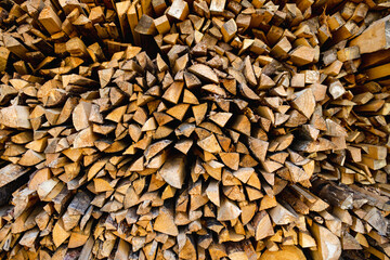 Tightly packed pile of split firewood arranged in an organic pattern, with earthy textures...