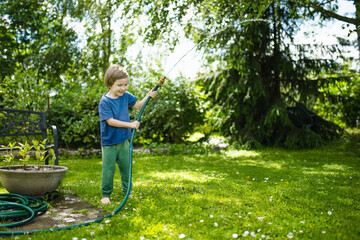 Cute little boy playing with garden hose on hot summer day. Child playing with water at summertime.