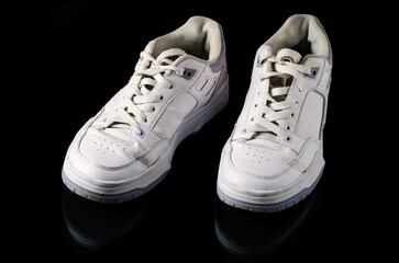 Old white sneakers with worn sole on black background