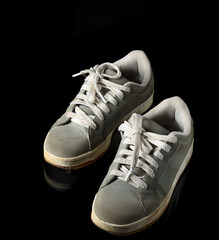 Old grey sneakers with worn fabric on black background