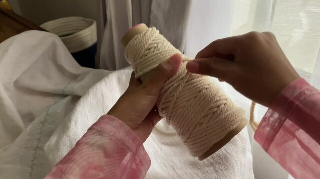 Close up of hands rolling cotton thread for macrame. Rolling thread in preparation for making macrame keychain, macrame accessories. Crafts and hobbies.