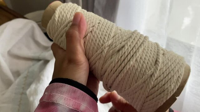 Close up of hands rolling cotton thread for macrame. Rolling thread in preparation for making macrame keychain, macrame accessories. Crafts and hobbies.
