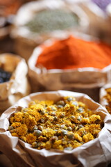 Colorful selection of dried herbs, spices, and natural ingredients in paper bags on rustic market table. Traditional Asian and herbal medicine concept.