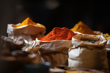 Colorful selection of dried herbs, spices, and natural ingredients in paper bags on rustic market table. Traditional Asian and herbal medicine concept.