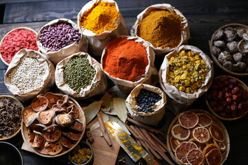Colorful selection of dried herbs, spices, and natural ingredients in paper bags on rustic market table. Traditional Asian and herbal medicine concept.