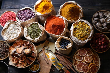 Colorful selection of dried herbs, spices, and natural ingredients in paper bags on rustic market table. Traditional Asian and herbal medicine concept.