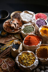 Colorful selection of dried herbs, spices, and natural ingredients in paper bags on rustic market table. Traditional Asian and herbal medicine concept.