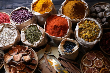 Colorful selection of dried herbs, spices, and natural ingredients in paper bags on rustic market table. Traditional Asian and herbal medicine concept.