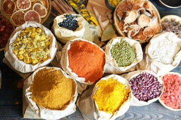 Colorful selection of dried herbs, spices, and natural ingredients in paper bags on rustic market table. Traditional Asian and herbal medicine concept.
