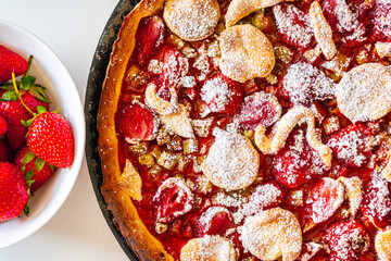 Rhubarb tart with strawberries and sugar on a white table. Traditional French dessert. Top view.