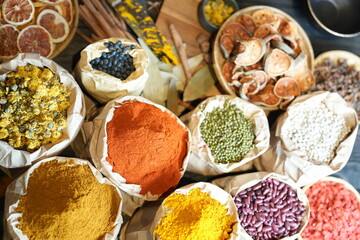 Colorful selection of dried herbs, spices, and natural ingredients in paper bags on rustic market...
