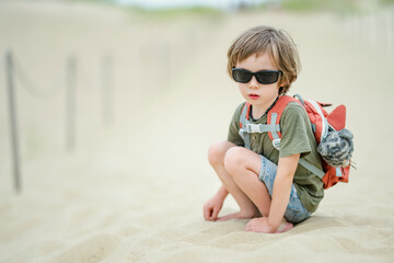 A cheerful child wearing sunglasses and a backpack running playfully on a wooden boardwalk at the Curonian Spit in Lithuania, enjoying an outdoor adventure.