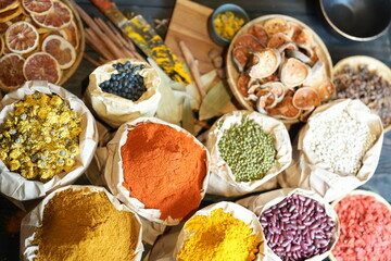 Colorful selection of dried herbs, spices, and natural ingredients in paper bags on rustic market table. Traditional Asian and herbal medicine concept.