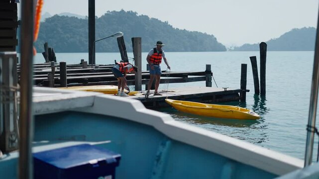 Two young men untying a yellow kayak from the dock before getting into the kayak