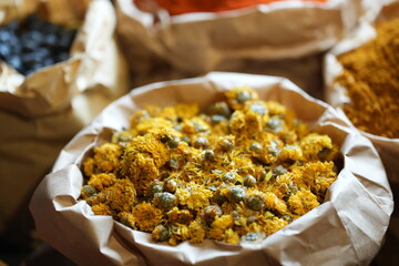 Colorful selection of dried herbs, spices, and natural ingredients in paper bags on rustic market table. Traditional Asian and herbal medicine concept.