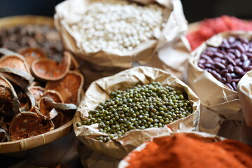 Colorful selection of dried herbs, spices, and natural ingredients in paper bags on rustic market table. Traditional Asian and herbal medicine concept.