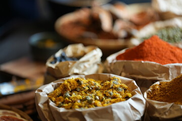 Colorful selection of dried herbs, spices, and natural ingredients in paper bags on rustic market table. Traditional Asian and herbal medicine concept.