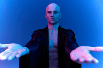 Man in a black robe extending his arms in a striking pose against a blue background, showcasing deep emotions and a dramatic atmosphere.