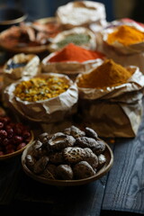 Colorful selection of dried herbs, spices, and natural ingredients in paper bags on rustic market table. Traditional Asian and herbal medicine concept.