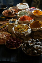 Colorful selection of dried herbs, spices, and natural ingredients in paper bags on rustic market table. Traditional Asian and herbal medicine concept.