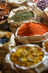 Colorful selection of dried herbs, spices, and natural ingredients in paper bags on rustic market table. Traditional Asian and herbal medicine concept.