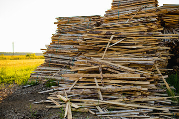 A loosely stacked pile of rough, uneven wood strips and bark-covered slats, wood offcuts or scrap material from milling or carpentry.